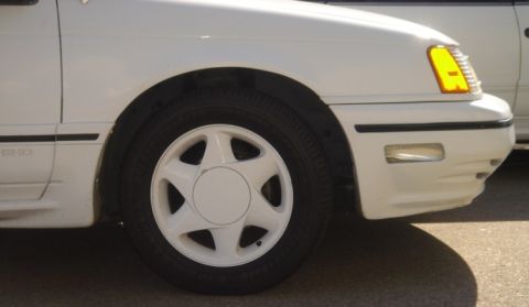 1991 Ford Taurus - A white 1991 Ford Taurus is shown from the front corner, revealing its wheel and headlight.