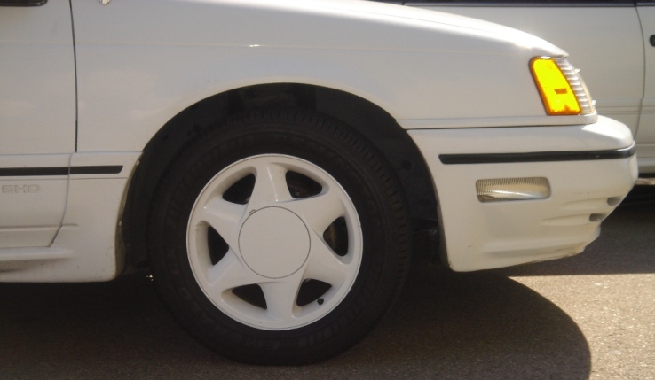 White 1991 Ford Taurus front corner with a five-spoke wheel and yellow turn signal