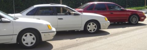 1991 Ford Taurus - Three sedans are parked on a street. The middle car is a 1991 Ford Taurus.