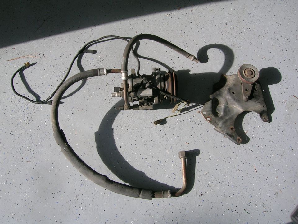A/C compressor with hoses, wiring, and mounting bracket with pulley laid on concrete floor