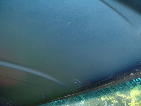1989 Ford Bronco - The interior ceiling of a vehicle is visible, with a reflection of the outdoors on the windshield.