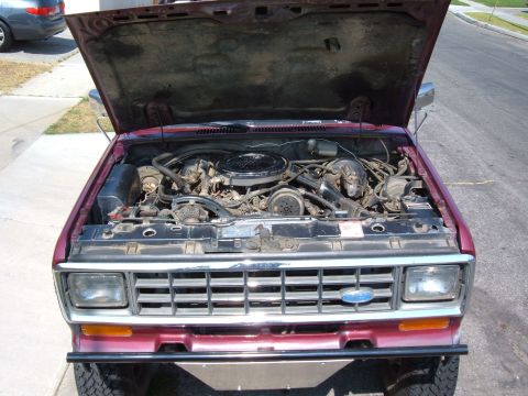 1985 Ford Bronco II - The engine bay of a 1985 Ford Bronco II is visible with the hood raised, showing the engine and surrounding components.