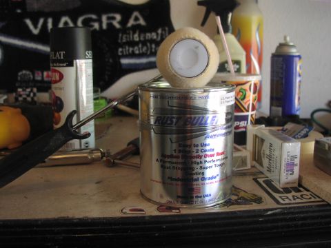 1979 Ford Bronco - A can of Rust Bullet coating and a paint roller sit on a cluttered workbench with other supplies.