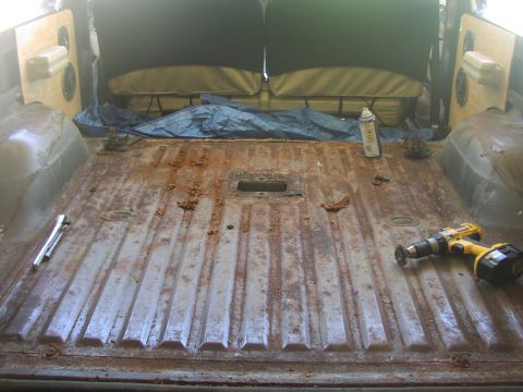 1979 Ford Bronco - The cargo area of a vehicle shows significant rust on the floor, with tools and a spray can present.