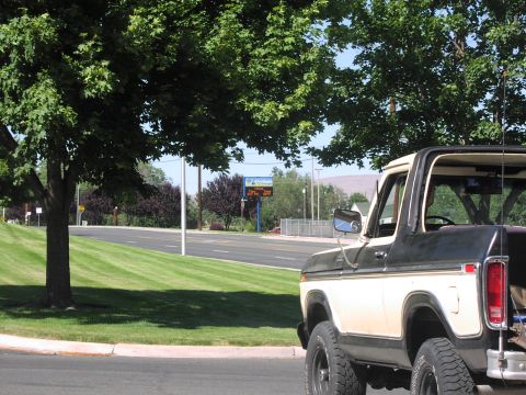 1979 Ford Bronco - This two-tone Ford Bronco is seen from the rear quarter, parked beside a road with trees and a digital sign in the background.