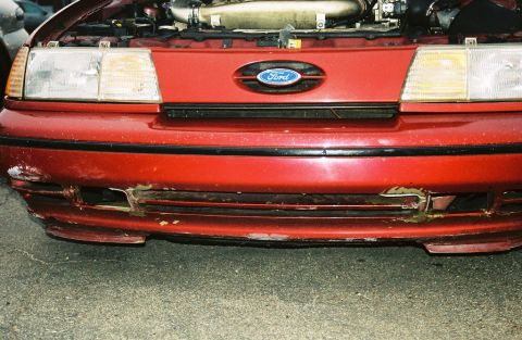 1991 Ford Taurus - Front view of a red 1991 Ford Taurus with a damaged bumper and the hood open.
