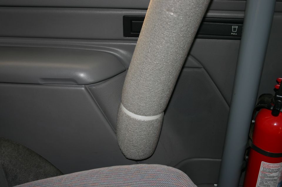 Gray SUV interior with foam-padded pillar, gray door panel, and red fire extinguisher