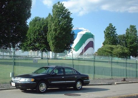 1997 Ford Crown Victoria - A black Lincoln Town Car is parked on the side of the road with a large, painted industrial tank in the background.