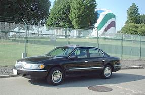 1997 Ford Crown Victoria - This black sedan, possibly a 1995 Lincoln Continental, is parked outdoors with a large, colorful cylindrical structure in the background.