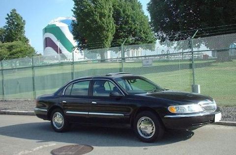 1997 Ford Crown Victoria - A black Lincoln Continental is parked near a fenced-off industrial area with a large, colorful silo.