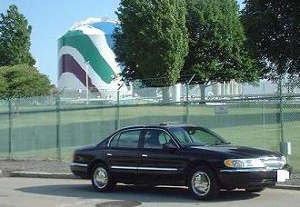 1997 Ford Crown Victoria - A black Lincoln Town Car is parked in front of a large, colorful industrial tank.