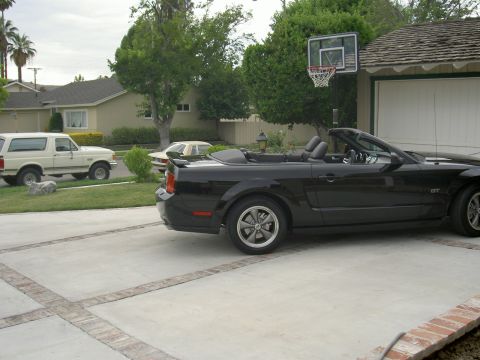 2005 Ford Mustang - A black convertible Mustang is parked in a driveway with a white SUV and a house in the background.