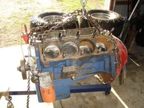 1963 Ford Galaxie - A V8 engine block, painted blue and red, is hoisted by chains with tires in the background.