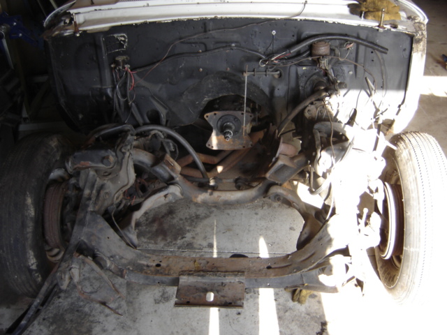 Empty engine bay of stripped classic car showing crossmember, control arms and bare firewall