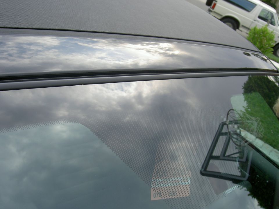 Black convertible top and windshield reflection of a 2005 Ford Mustang. Another vehicle is visible in the background