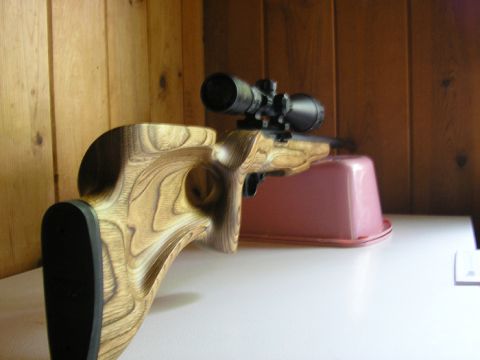 1990 Ford Probe - A rifle with a wooden stock and a scope is displayed on a white surface against a wood-paneled wall.