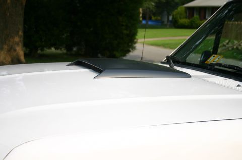 1994 Ford Bronco - A black hood scoop is mounted on the hood of a white vehicle, with a residential background.