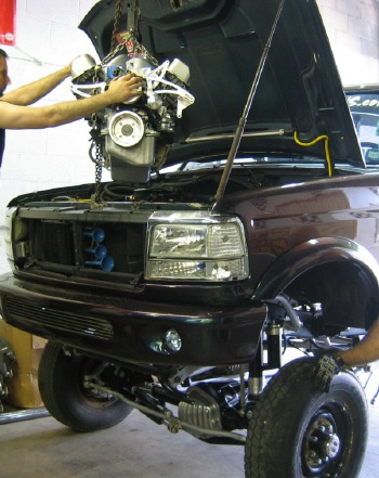 1994 Ford Bronco - Mechanics are installing a new engine into the front of a truck.