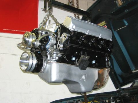1994 Ford Bronco - Engine assembly with chrome valve covers and black block, suspended by chains for installation.