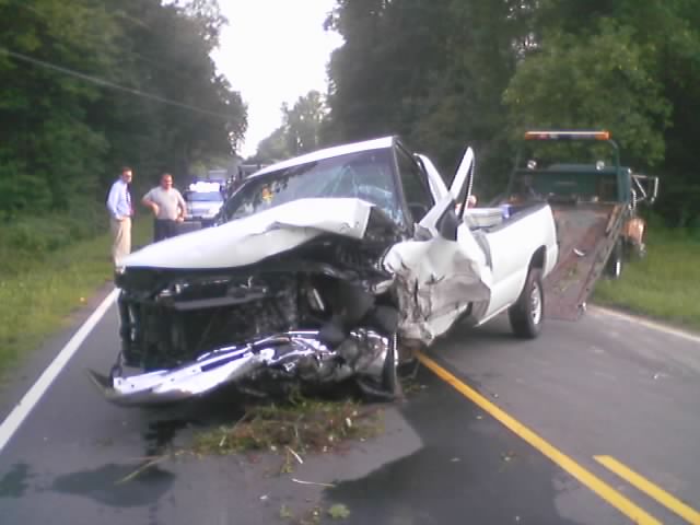 White pickup with severe driver-side front-end crash damage on rural road