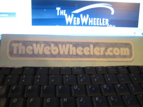 1990 Ford Bronco - frosted TheWebWheeler.com sticker sits on a laptop above the keyboard, with the site's logo on screen behind it.