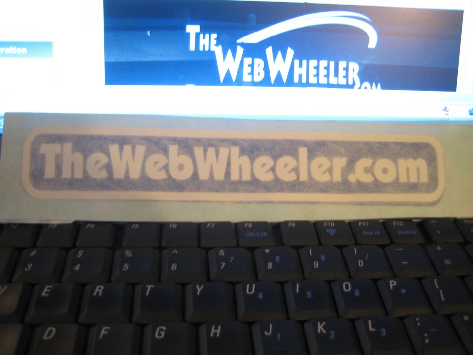 TheWebWheeler.com decal on a laptop above its keyboard and logo screen