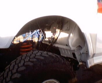 1981 Ford Bronco - Close-up view of the front wheel well and suspension system of a white vehicle, revealing an orange coil spring.