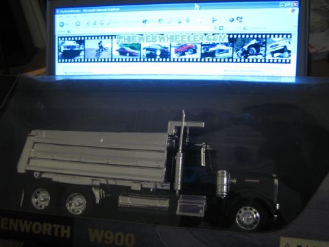 1990 Ford Bronco - black Kenworth W900 dump-truck die-cast model sits in its box in front of a laptop showing TheWebWheeler.com.