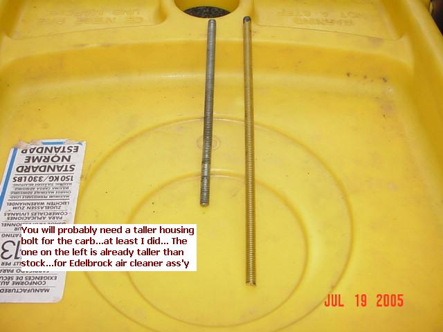 Two threaded carburetor studs on yellow surface with handwritten note about taller housing bolt