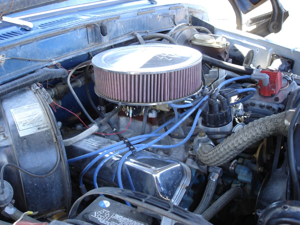 Engine bay with large circular air filter, blue spark plug wires, and distributor cap