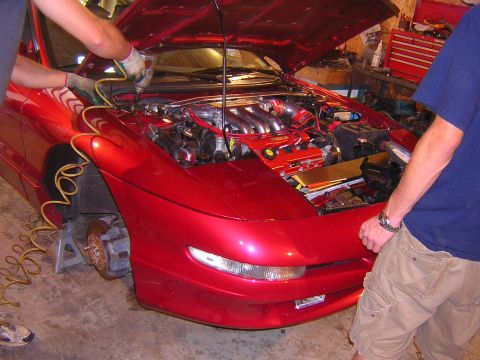 1995 Ford Probe - Mechanics work on the engine of a red 1995 Ford Probe in a garage setting.