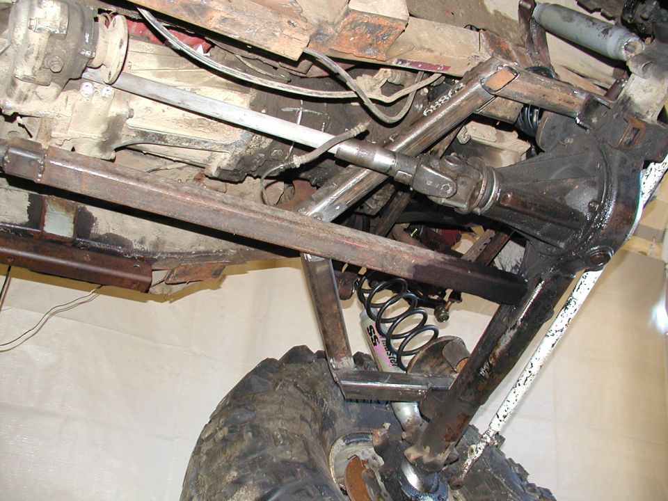 Underside of Suzuki Samurai showing custom link suspension, coil spring, driveshaft, axle and off-road tire