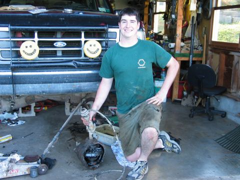 1995 Ford Bronco - A person in a green T-shirt kneels on a garage floor beside a front axle center section pulled from the truck, with the differential, ring…