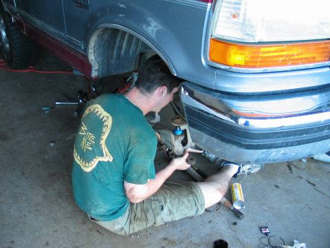 1995 Ford Bronco - A person is performing maintenance on the front suspension of a vehicle, likely a truck or SUV.