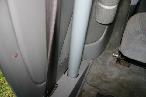 1994 Ford Bronco - Close-up of a gray vehicle interior showing the B-pillar area with a seat belt, a vertical gray grab handle or rail, and a fabric-trimmed p…