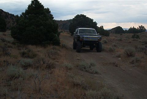 1986 Ford Bronco - A lifted black Ford Bronco sits on a dirt road in a dry, hilly landscape under a cloudy sky.