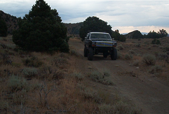 Lifted black Ford Bronco on a dirt road with trees and hills in the background