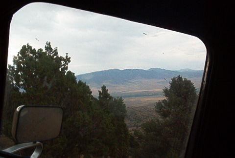 1986 Ford Bronco - View from inside a vehicle shows a side mirror and a vast landscape with mountains under a cloudy sky.