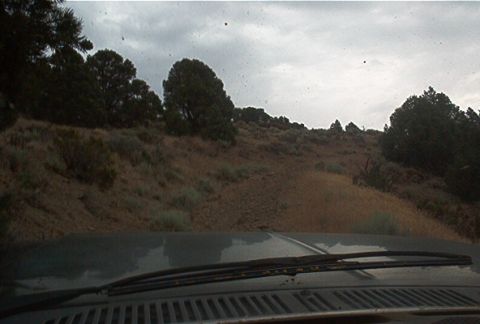 1986 Ford Bronco - View from inside a vehicle as it travels along a dirt road through a dry, hilly landscape.
