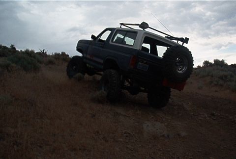1986 Ford Bronco - Modified 1986 Ford Bronco tackling an off-road trail under a cloudy sky.