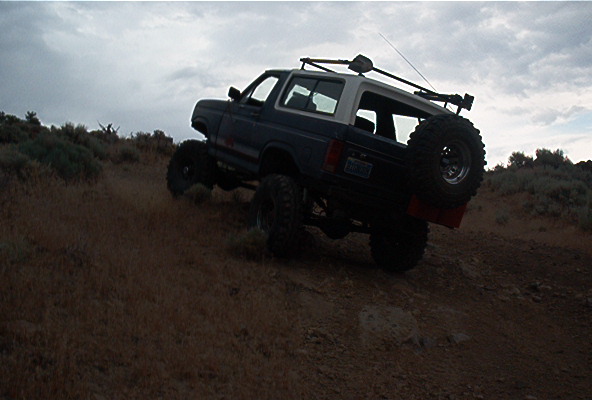 1986 Ford Bronco climbing a dirt hill with a spare tire mounted on the rear
