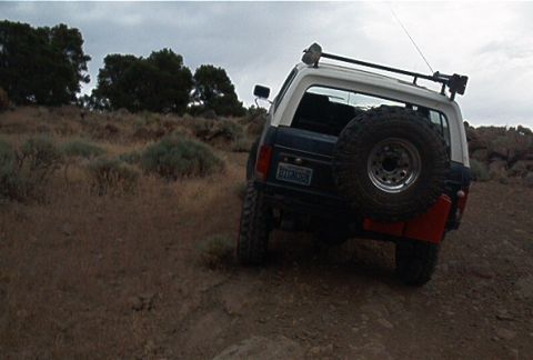 1986 Ford Bronco - The 1986 Ford Bronco navigates a rocky, off-road terrain under a cloudy sky.