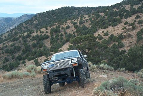 1986 Ford Bronco - 1986 Ford Bronco navigates a rough dirt trail in a mountainous, scrub-covered area.