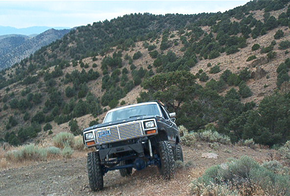 1986 Ford Bronco driving on a dirt road in a hilly, arid landscape