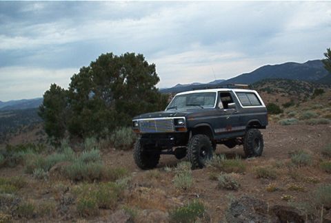 1986 Ford Bronco - This lifted 1986 Ford Bronco is parked on a dry, hilly terrain under a cloudy sky.
