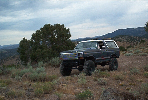 Dark blue 1986 Ford Bronco with white top and off-road tires on a dusty hill