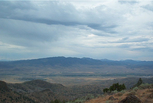 Mountain range under cloudy sky, with foreground scrub and a Supermotors watermark