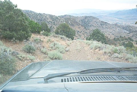 1986 Ford Bronco - View from inside a vehicle driving on a dirt road through a mountainous, dry terrain.
