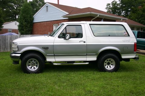 1994 Ford Bronco - Side profile of a 1994 Ford Bronco with two-tone paint, parked on a grassy lawn.