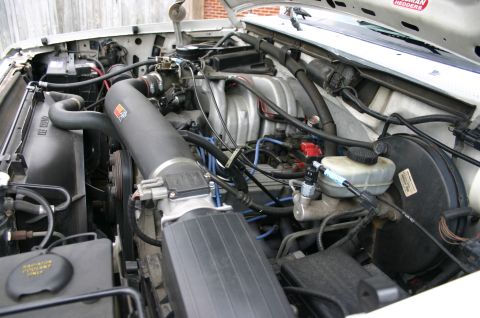 1994 Ford Bronco - Engine bay of a fuel-injected Ford V8 with an aftermarket black air-intake tube, blue spark-plug wires and a 'Hedman Hedders' sticker on th…